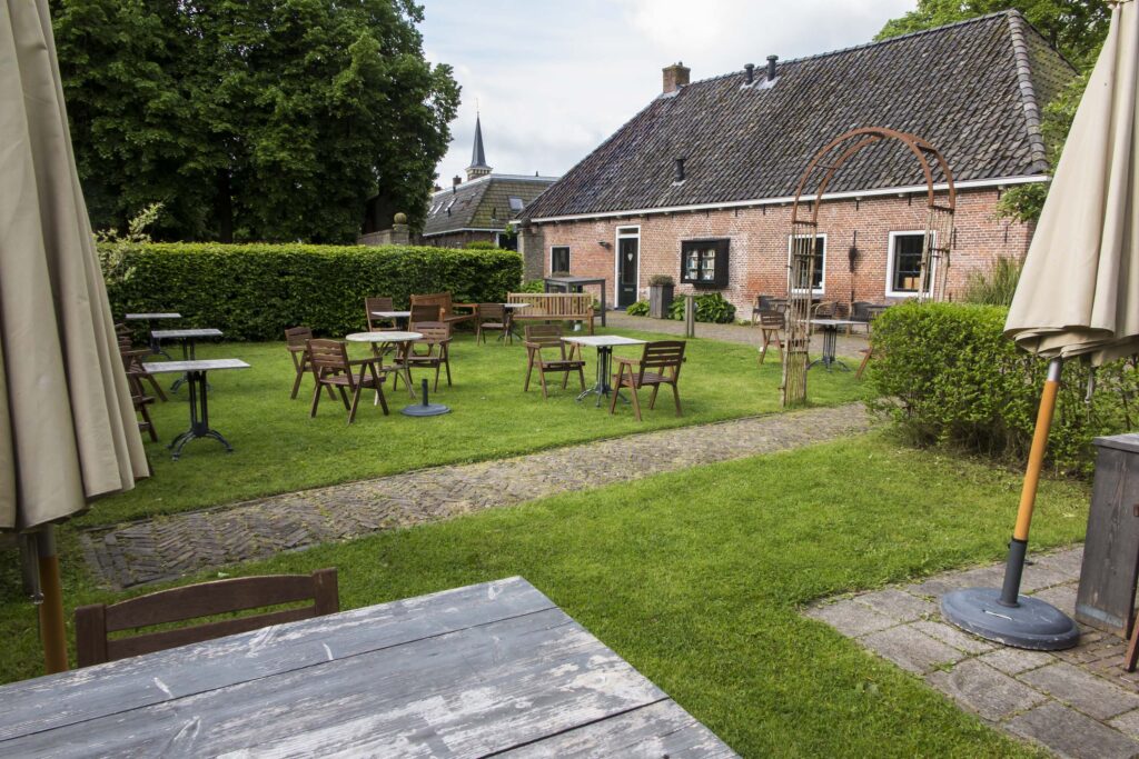 De theetuin van Túnmanswente met houten stoelen en parasols, en het oude tuinmanshuis op de achtergrond.